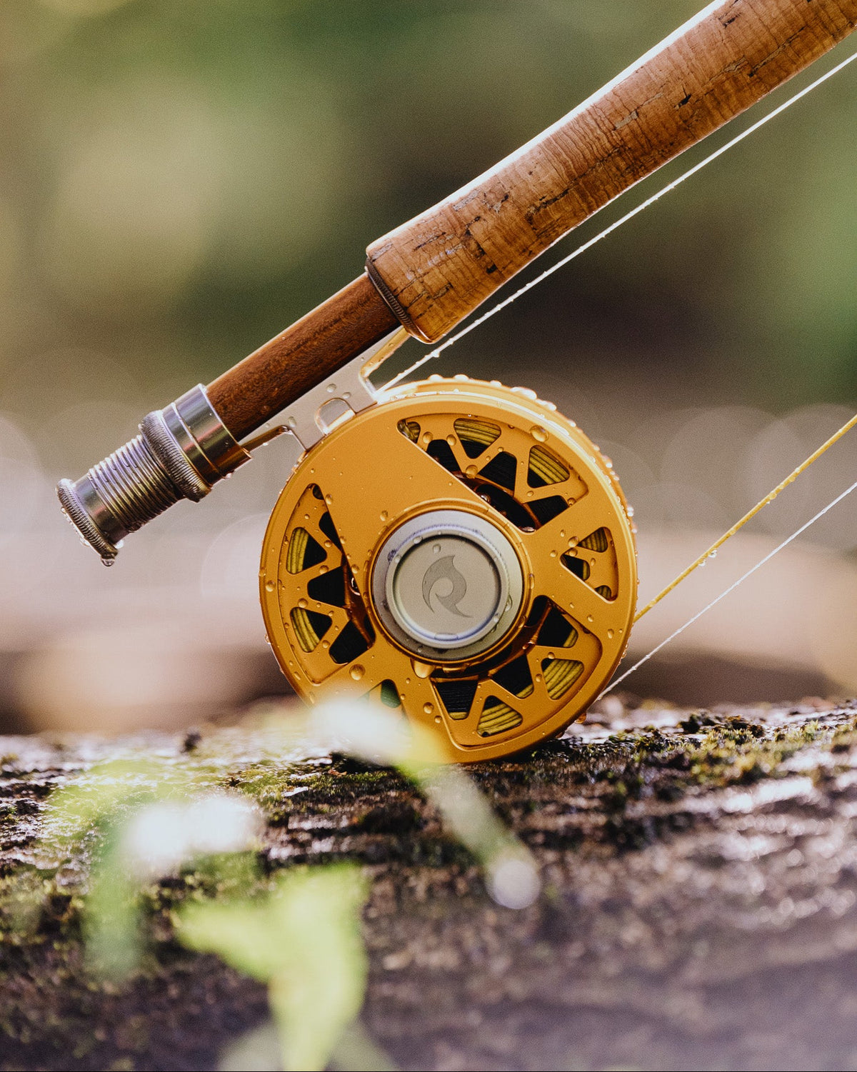 Vernly Series Stone fly reel in Solar Orange mounted on a bamboo rod, resting on a mossy log